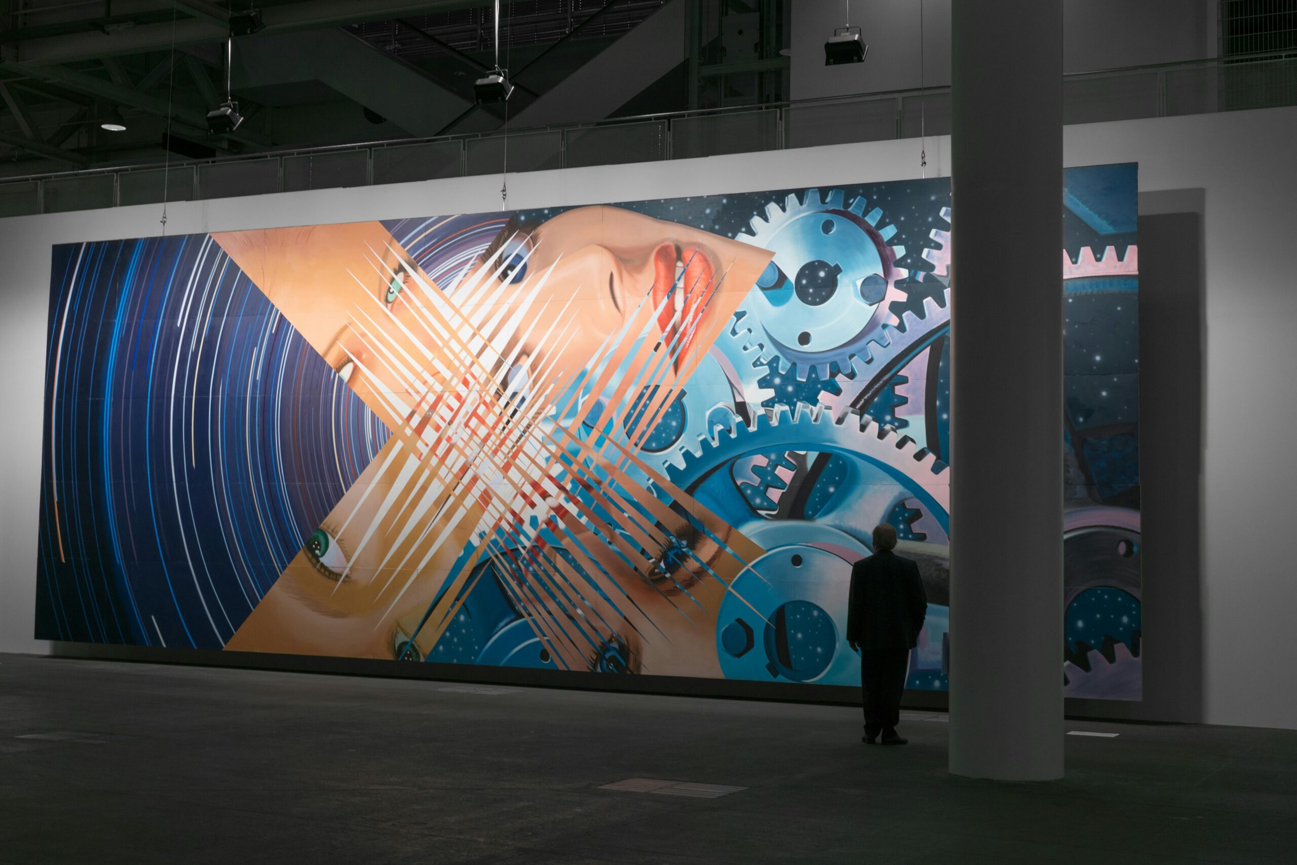 A large futuristic artwork depicting gears and a face in a contemporary gallery setting.